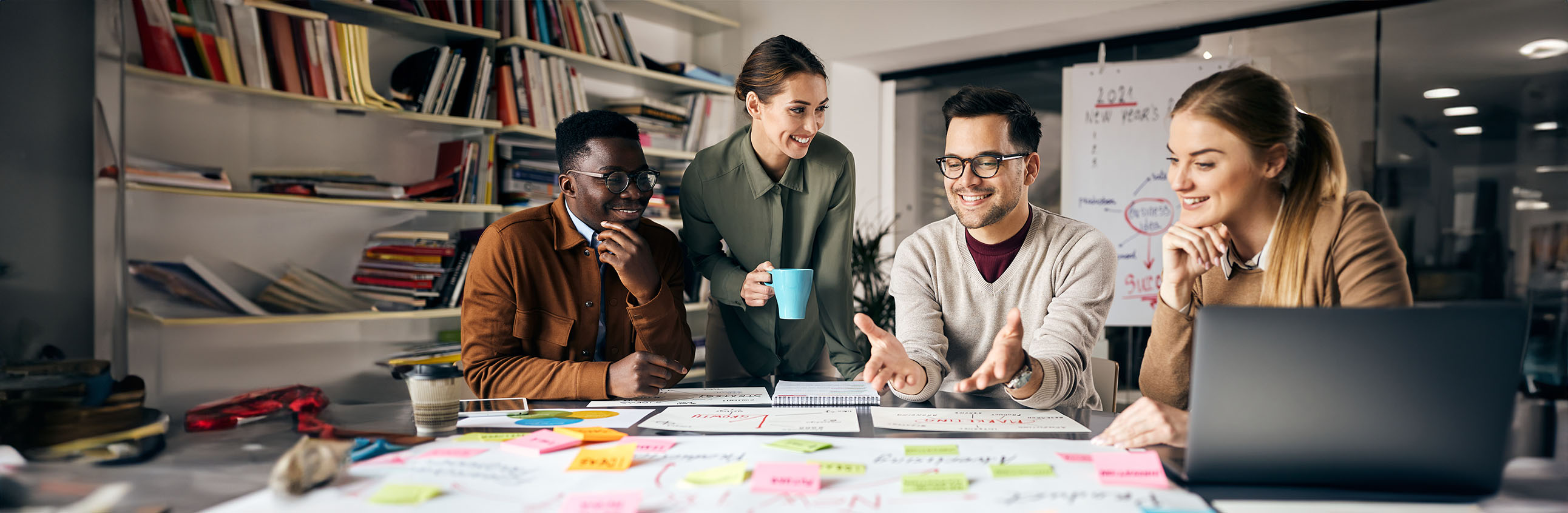 Kollaboratives Arbeiten im Fokus: Vier engagierte Personen setzen sich gemeinsam für ein Projekt ein. Umgeben von Büchern, Notizen, einer Flipchart und einem Laptop demonstrieren sie effektive Zusammenarbeit. Dies unterstreicht die bedeutsamen Kooperationen von Masters of Marketing mit Arbeitgebern im Bereich des Online-Marketings.